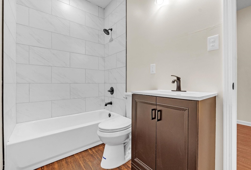 Bathroom featuring wood finished floors, vanity, toilet, and  shower combination