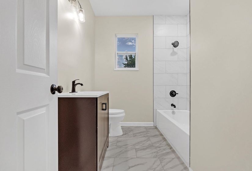 Bathroom with marble finish flooring, toilet, vanity, tub / shower combination, and baseboards