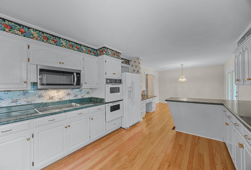 Kitchen with white appliances, pendant lighting, kitchen peninsula, light hardwood / wood-style floors, and white cabinetry