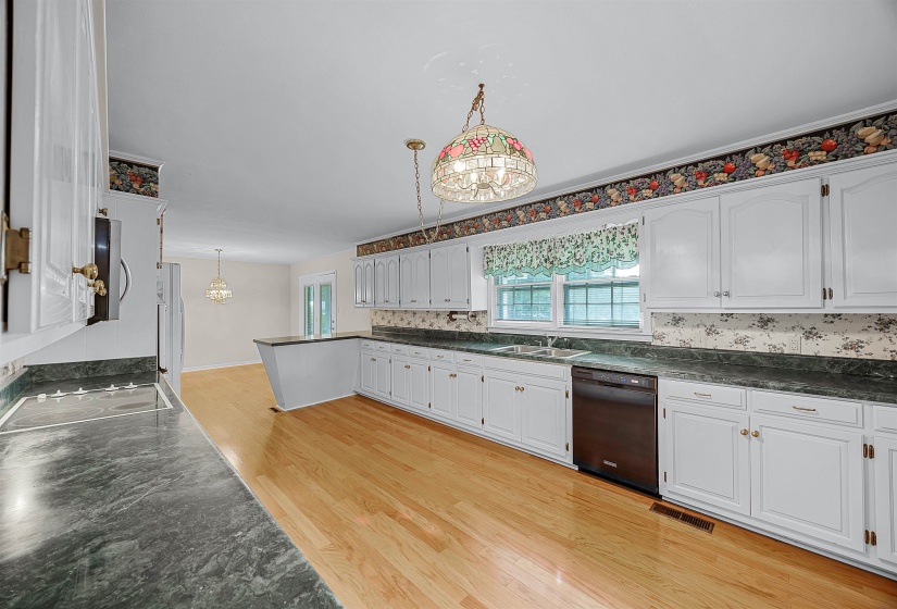 Kitchen featuring black dishwasher, hanging light fixtures, light wood-type flooring, and white cabinets