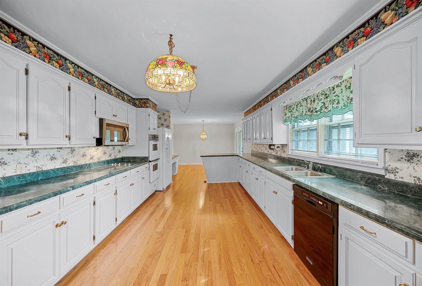 Kitchen with white cabinetry, pendant lighting, sink, black dishwasher, and light hardwood / wood-style flooring