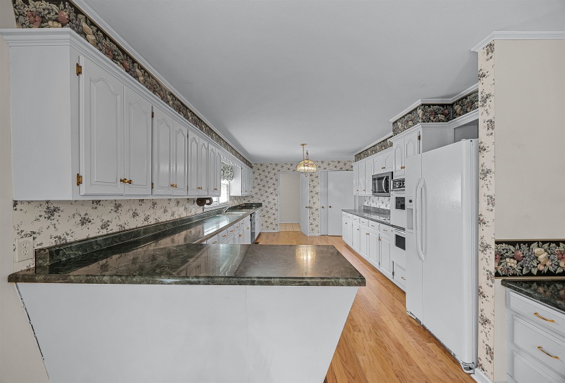 Kitchen featuring white cabinets, ornamental molding, white refrigerator with ice dispenser, light hardwood / wood-style flooring, and kitchen peninsula
