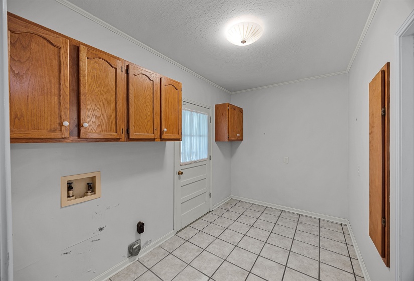 Clothes washing area featuring hookup for a washing machine, cabinets, light tile patterned floors, a textured ceiling, and ornamental molding