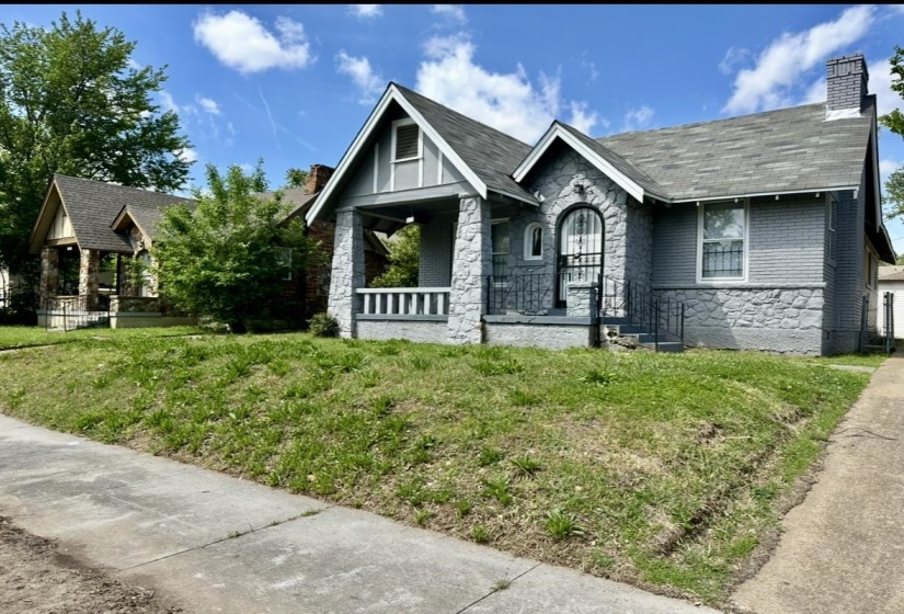 Tudor home with stone siding, a chimney, covered porch, and a front lawn
