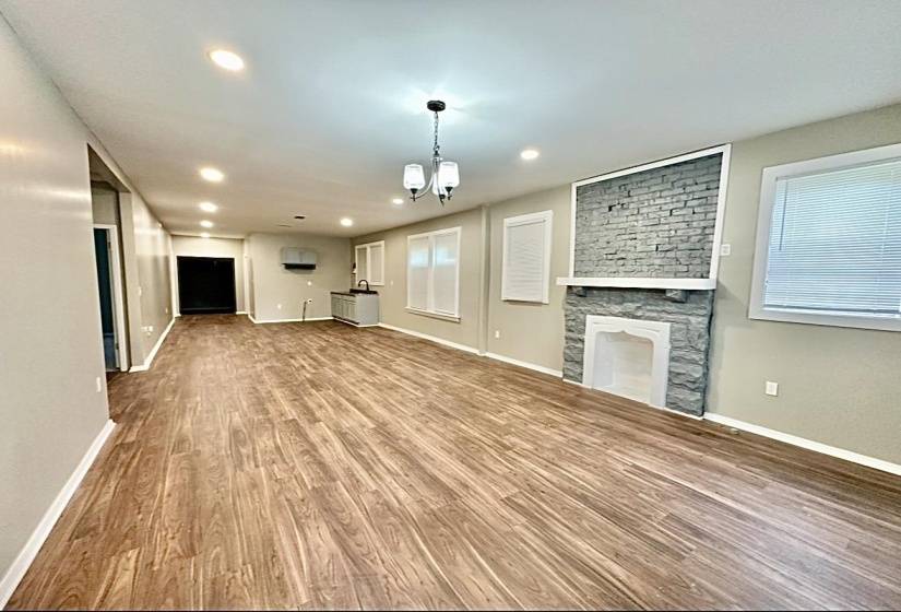 Unfurnished living room featuring wood finished floors, a chandelier, baseboards, recessed lighting, and a large fireplace
