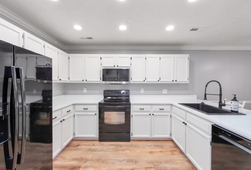 Kitchen with white cabinets, a sink, black appliances, and light wood-type flooring