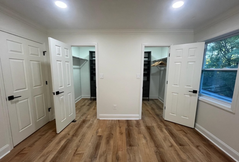 Unfurnished bedroom with a closet, crown molding, baseboards, wood finished floors, and a walk in closet