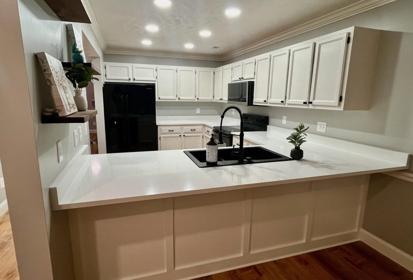 Kitchen featuring crown molding, a sink, a peninsula, black refrigerator with ice dispenser, and stainless steel microwave