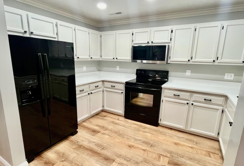 Kitchen featuring crown molding, light countertops, white cabinetry, light wood-type flooring, and black appliances