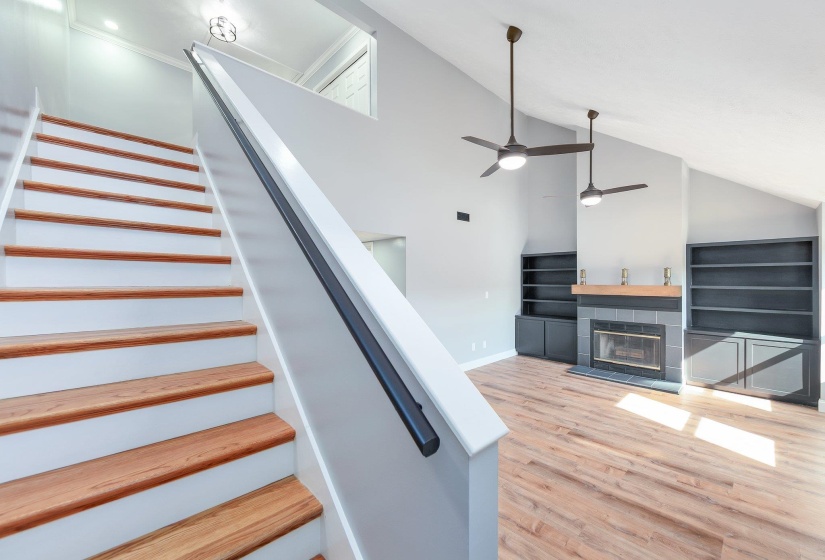 Staircase featuring high vaulted ceiling, baseboards, ceiling fan, a fireplace, and wood finished floors