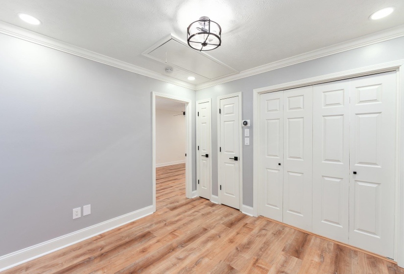 Unfurnished bedroom featuring attic access, baseboards, crown molding, and light wood-style floors