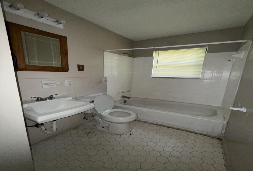 Bathroom featuring bathing tub / shower combination, toilet, a sink, and tile walls