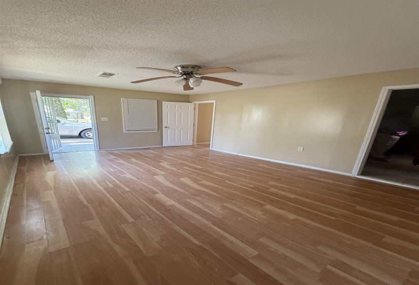 Unfurnished living room featuring light wood-style flooring, ceiling fan, a textured ceiling, and baseboards