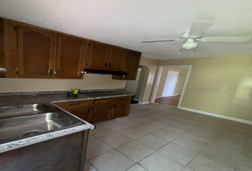 Kitchen with a ceiling fan, black electric stovetop, a textured ceiling, baseboards, and a sink
