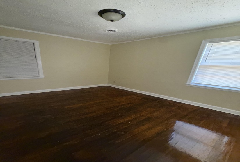 Empty room featuring dark wood-style flooring, ornamental molding, a textured ceiling, and baseboards