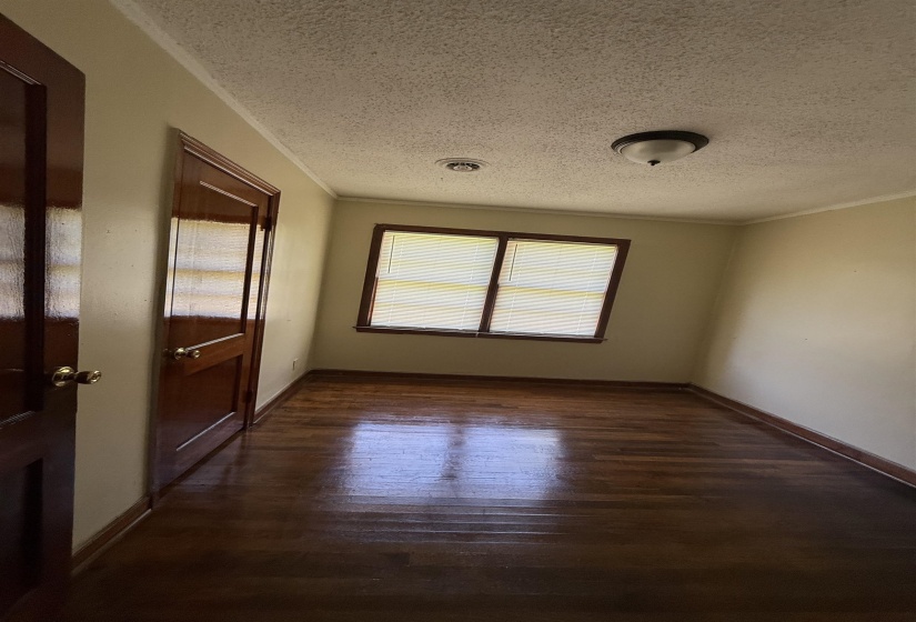 Spare room with crown molding, a textured ceiling, wood finished floors, and baseboards