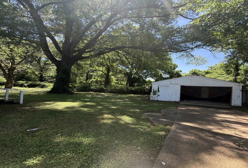 View of green lawn with a garage, an outbuilding, and driveway