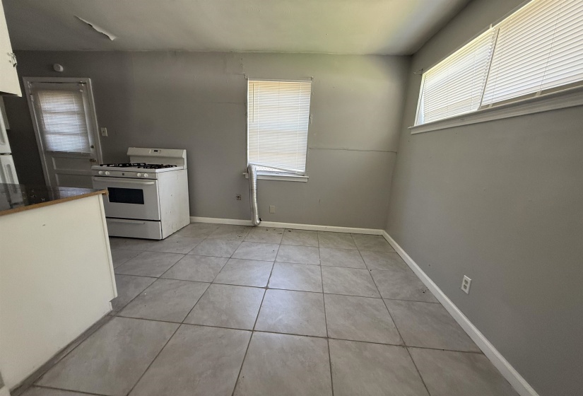 Kitchen featuring white range with gas cooktop, light tile patterned flooring, dark countertops, white cabinets, and baseboards