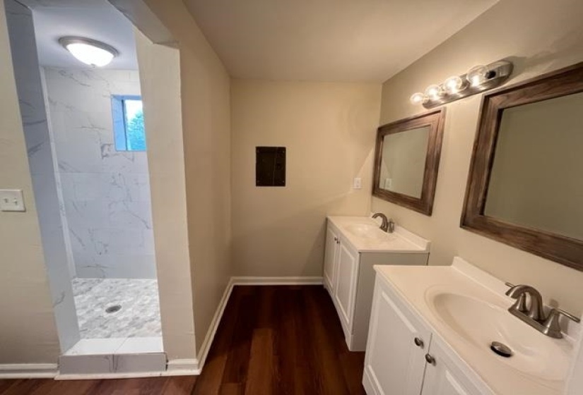 Bathroom with a marble finish shower, wood finished floors, two vanities, and baseboards