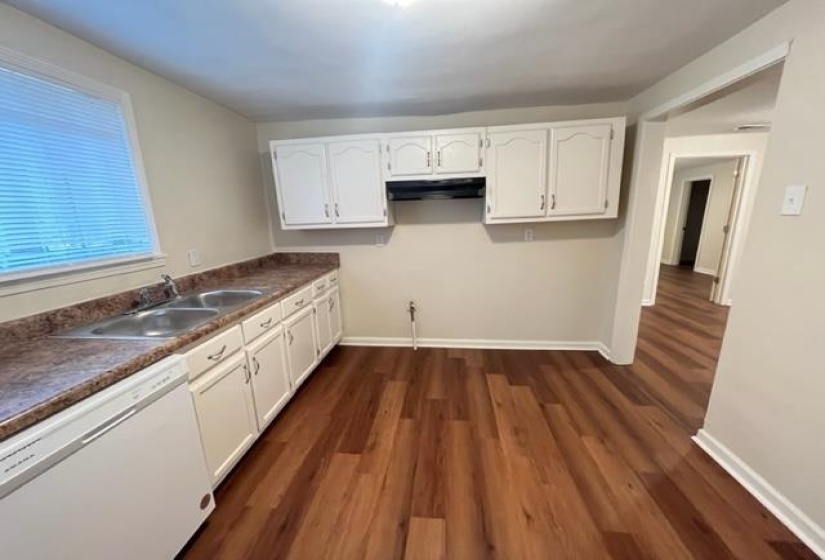 Kitchen featuring white dishwasher, a sink, under cabinet range hood, white cabinets, and dark wood-style floors