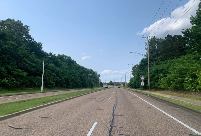 View of asphalt road featuring street lighting, traffic signs, and curbs