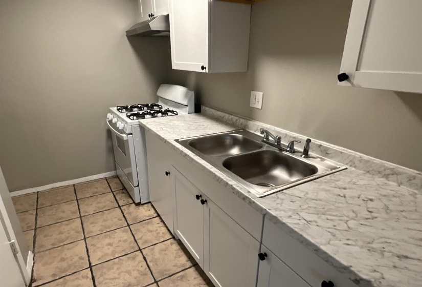 Kitchen featuring gas range gas stove, a sink, under cabinet range hood, light tile patterned floors, and light countertops