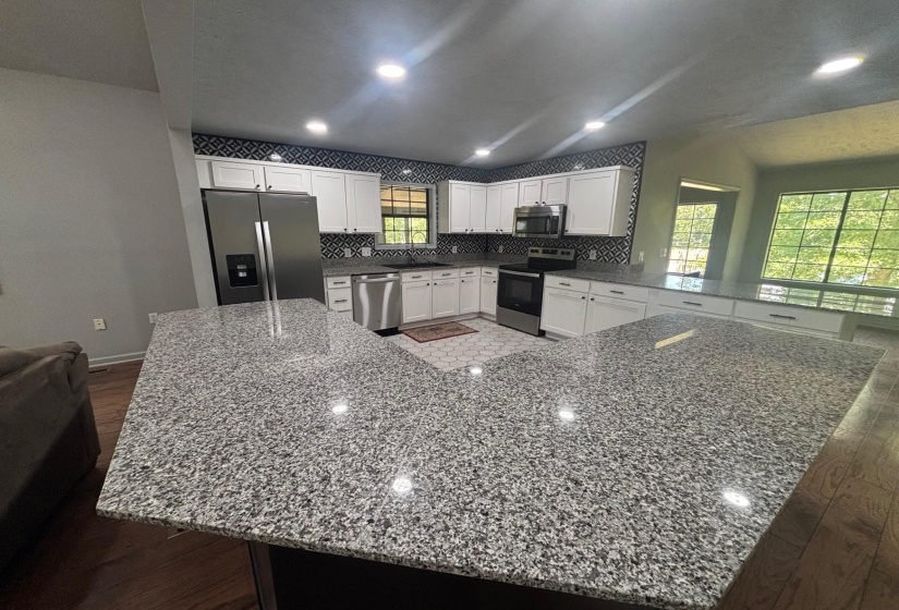 Kitchen featuring stainless steel appliances, wood finished floors, a peninsula, white cabinetry, and recessed lighting