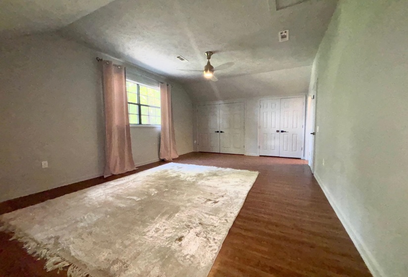 Spacious upstairs bedroom with ensuite bath, lofted ceiling, a ceiling fan, baseboards, and wood finished floors