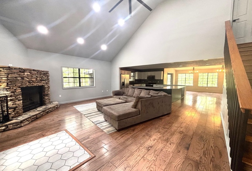 Living area with high vaulted ceiling, a stone fireplace, and wood-type flooring