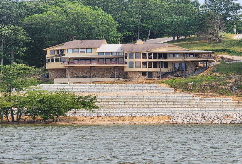 Back of property featuring a chimney, a deck with water view, and stone siding