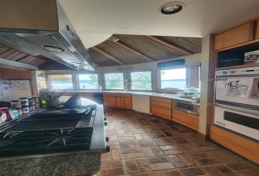 Kitchen featuring white dishwasher, double wall oven, stainless steel microwave, brick floors, and ventilation hood