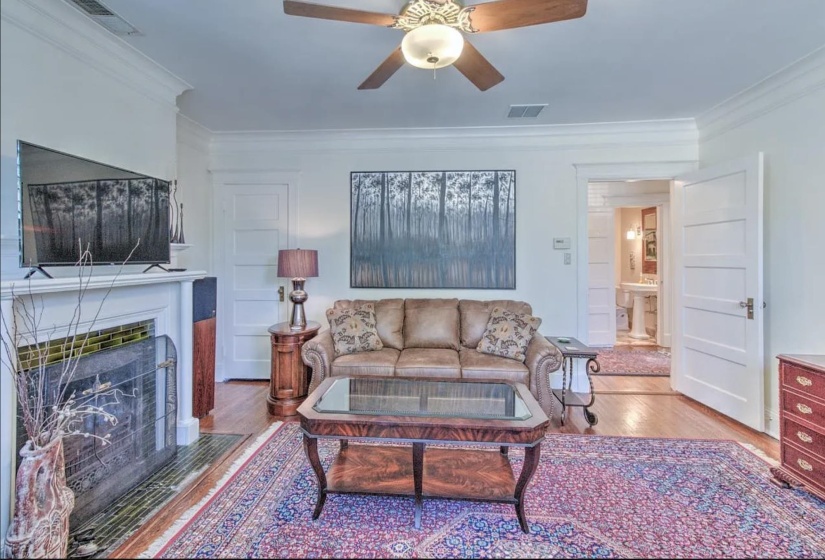 Living room featuring wood finished floors, ceiling fan, crown molding, and a fireplace with flush hearth