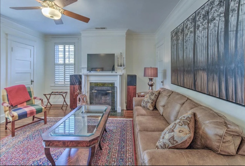 Living room with a fireplace with flush hearth, a ceiling fan, wood finished floors, ornamental molding, and baseboards