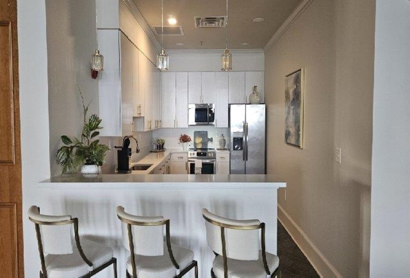 Kitchen with appliances with stainless steel finishes, a sink, ornamental molding, a peninsula, and baseboards