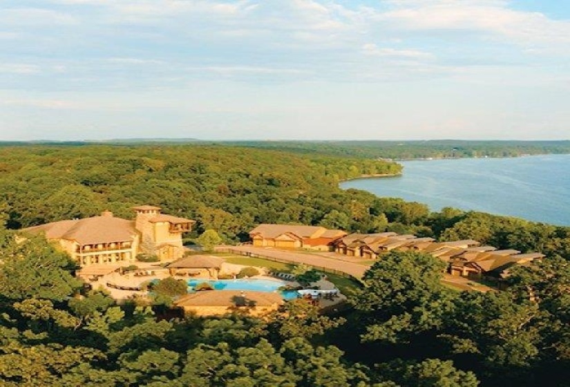 View from above of property with a heavily wooded area, a large body of water, and a pool