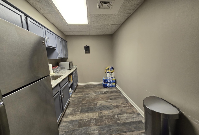 Kitchen featuring freestanding refrigerator, dark wood-style flooring, a drop ceiling, baseboards, and gray cabinetry
