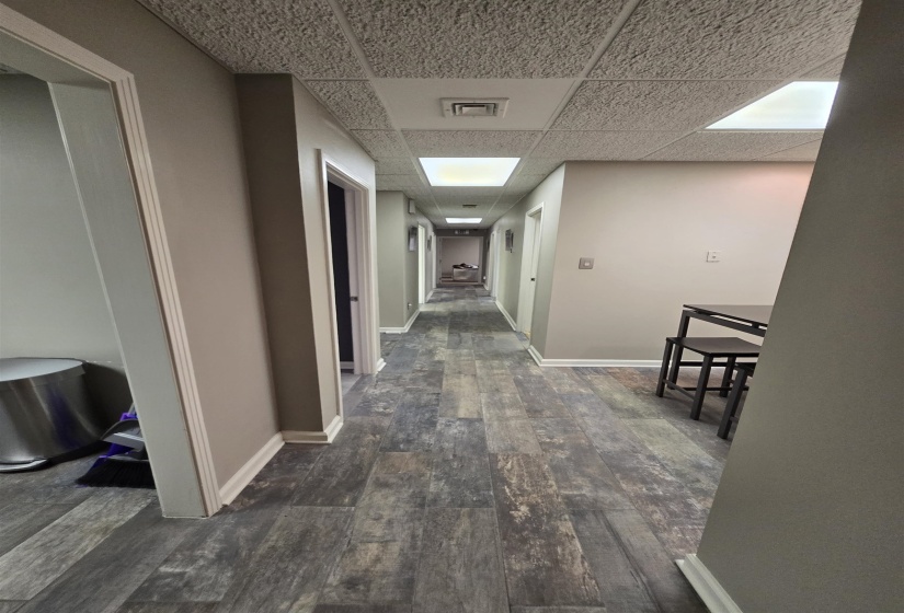Hall with wood-type flooring, a paneled ceiling, and baseboards