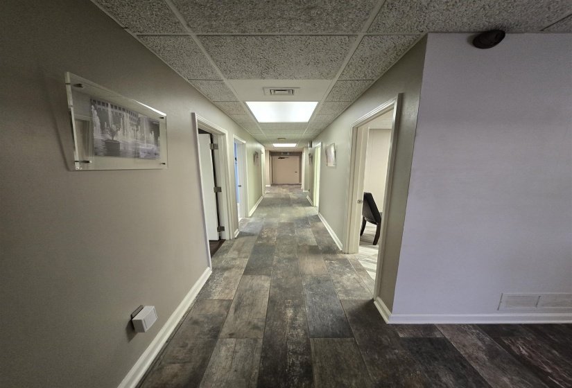 Corridor with a drop ceiling, dark wood-style flooring, and baseboards