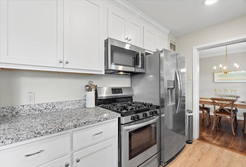 Kitchen with appliances with stainless steel finishes, a chandelier, light wood-style floors, white cabinetry, and light stone counters