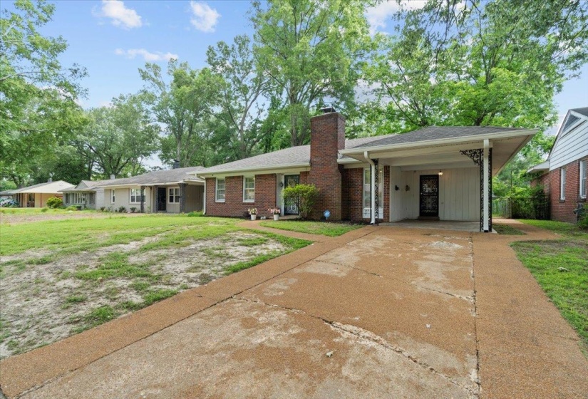 Ranch-style house featuring driveway, a chimney, a front lawn, a carport, and brick siding