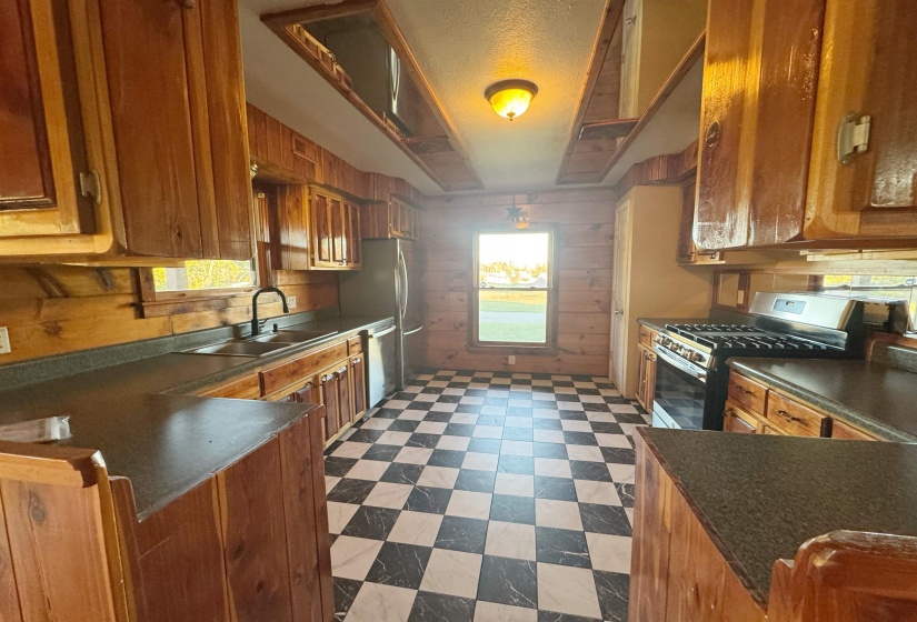 Kitchen featuring wooden walls, dark floors, brown cabinets, appliances with stainless steel finishes, and dark countertops