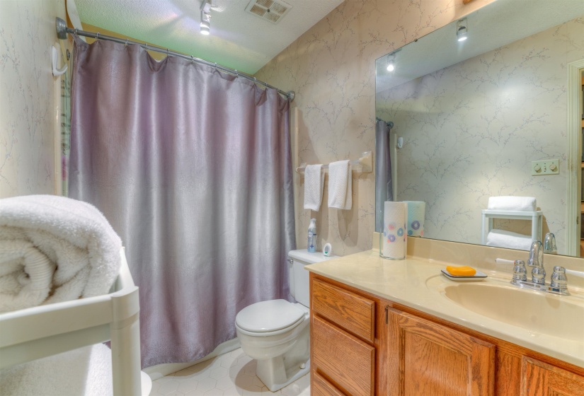 Full bath with toilet, wallpapered walls, vanity, and curtained shower