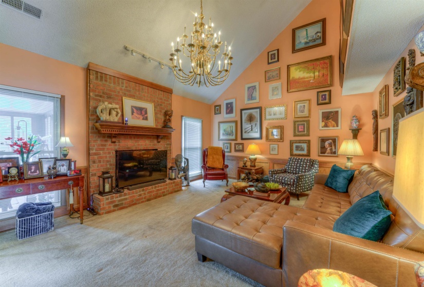 Living area featuring a brick fireplace, carpet, a chandelier, and high vaulted ceiling
