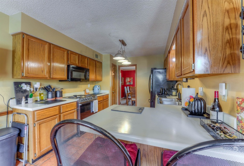Kitchen with black appliances, a sink, brown cabinetry, light countertops, and a peninsula
