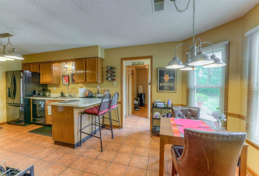 Kitchen featuring black appliances, brown cabinetry, light tile patterned floors, a peninsula, and a textured ceiling