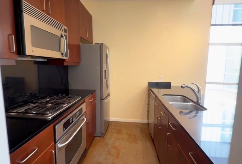 Kitchen featuring appliances with stainless steel finishes, dark countertops, brown cabinetry, and a peninsula