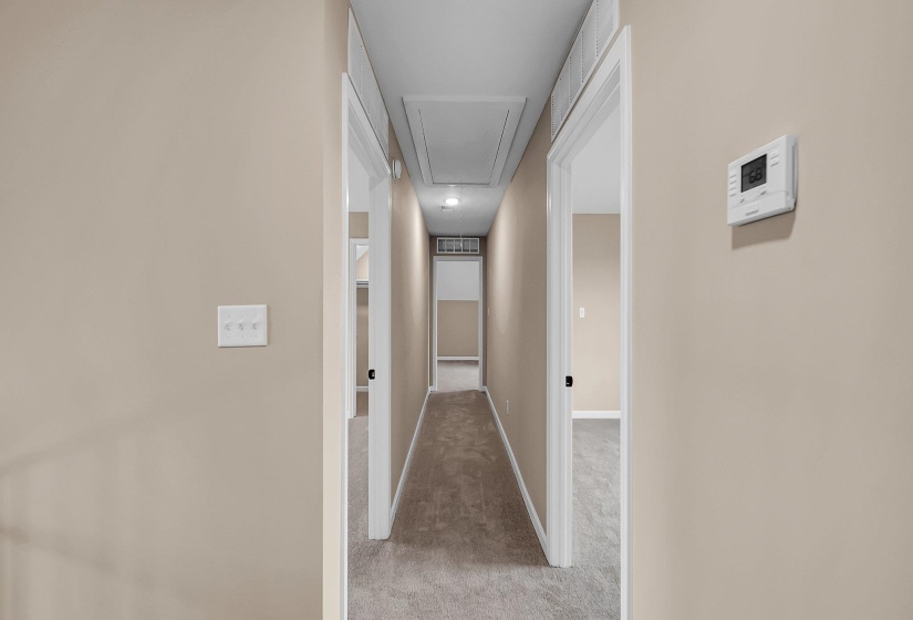 Hallway featuring light carpet, attic access, visible vents, and baseboards