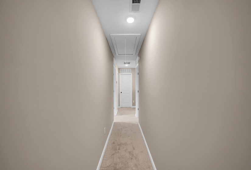 Corridor featuring light carpet, attic access, visible vents, and baseboards