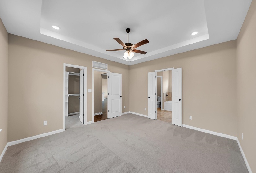 Unfurnished bedroom featuring light carpet, a tray ceiling, visible vents, and baseboards
