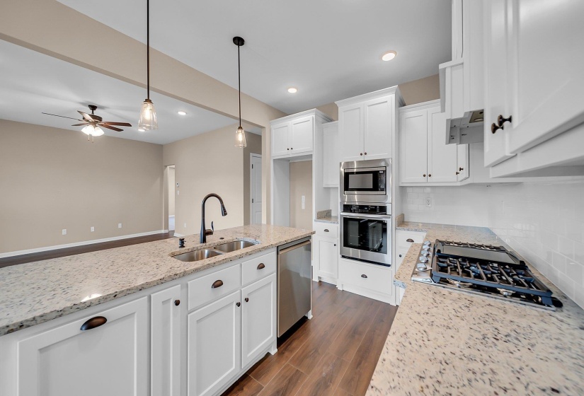 Kitchen featuring white cabinets, light stone counters, stainless steel appliances, pendant lighting, and a sink